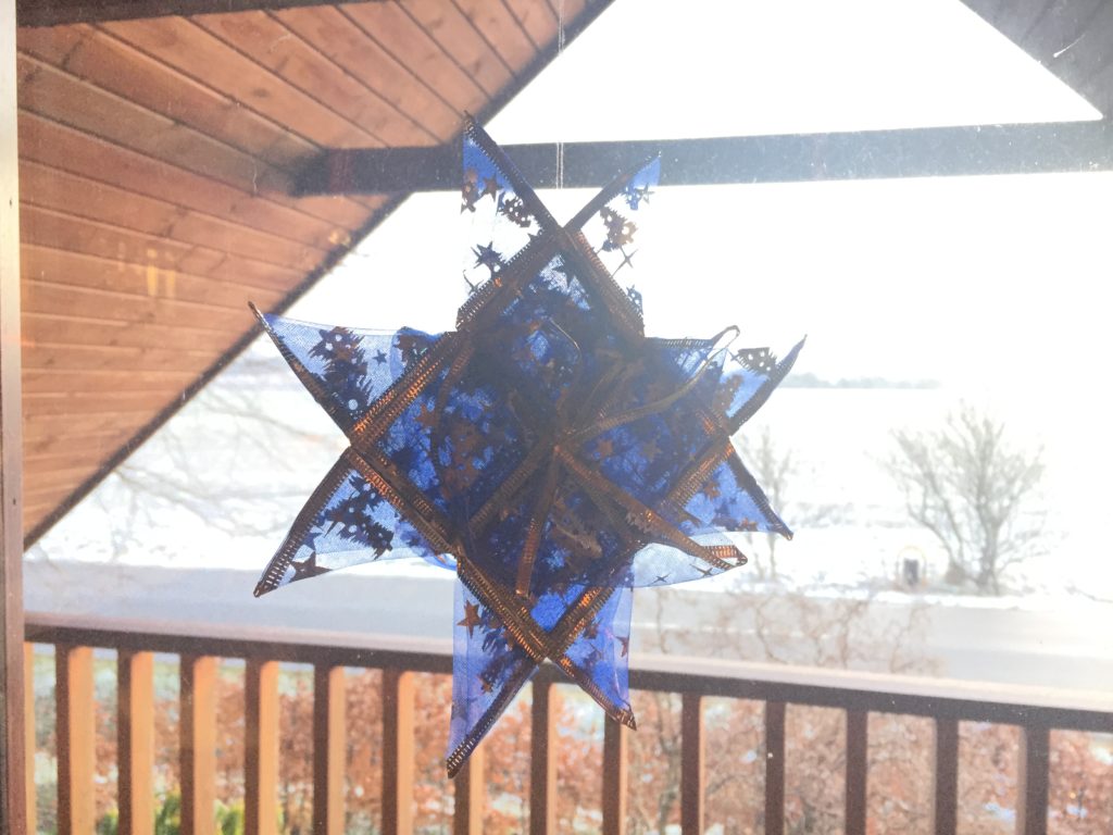 Flettet stjerne i krølbånd i vinduet med sne og sol